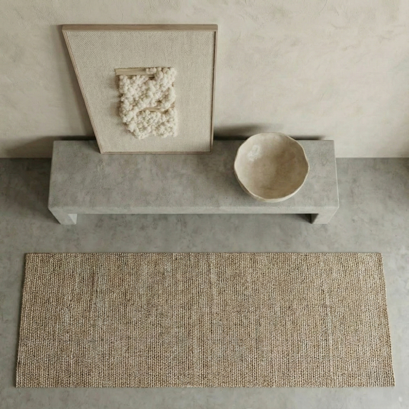 Beige woven rug on a concrete floor with a stone bench and bowl in the background.
