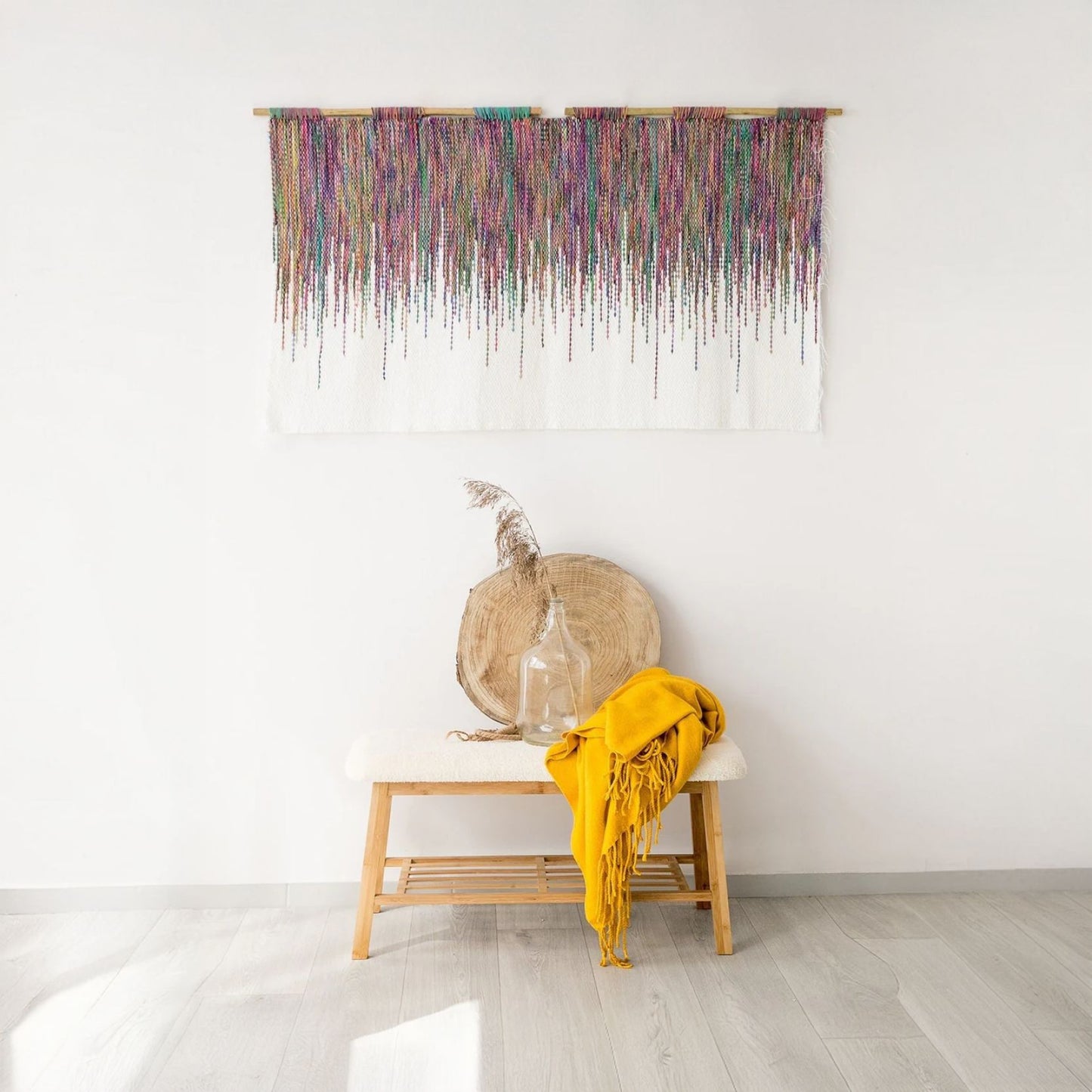 Colora tapestry featuring vibrant cascading threads of colorful acrylic yarn on a white background, suspended on a bamboo rod, perfect for boho and modern interiors.
