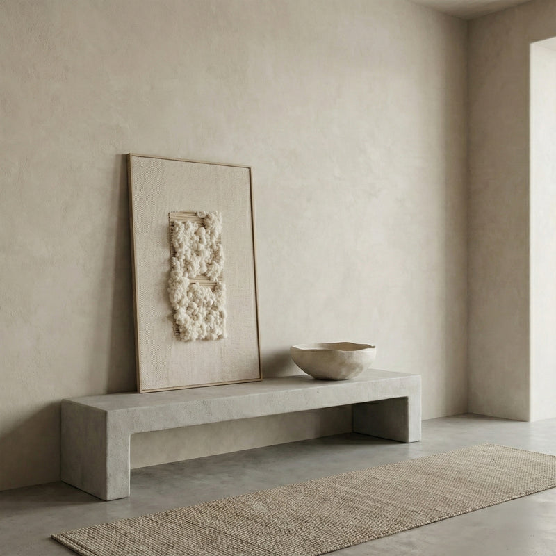 Minimalist interior with a concrete bench, textured wall art, and woven rug.