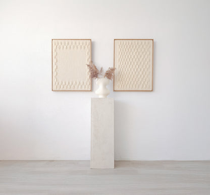 Set of two handcrafted minimalist wall hangings in neutral tones, framed in natural wood, displayed with a modern vase on a pedestal.