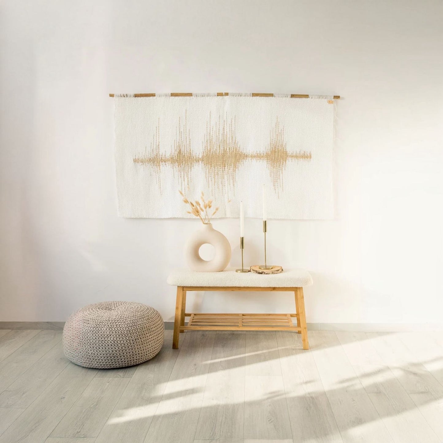 Handwoven wall tapestry featuring a gold soundwave pattern on a white background, crafted from wool and displayed in a modern interior with minimalist decor accents.